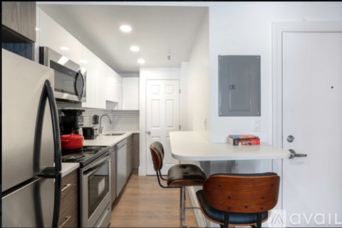 A kitchen with a refrigerator, oven, and a dining table with a chair.