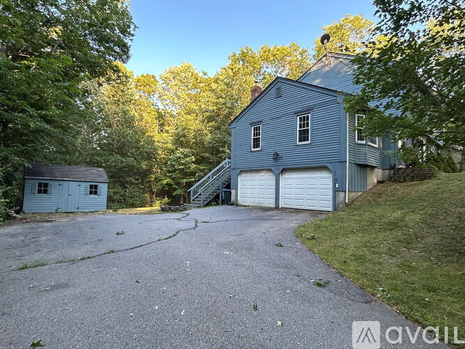 A large blue barn with a white garage door is surrounded by trees.