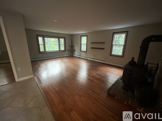 A spacious room with wooden floors and three windows.