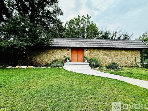 A stone building with a red door is surrounded by greenery.