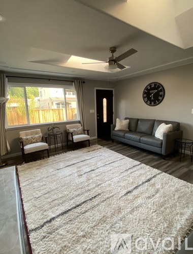 A living room with a grey couch, a white rug, and a ceiling fan.
