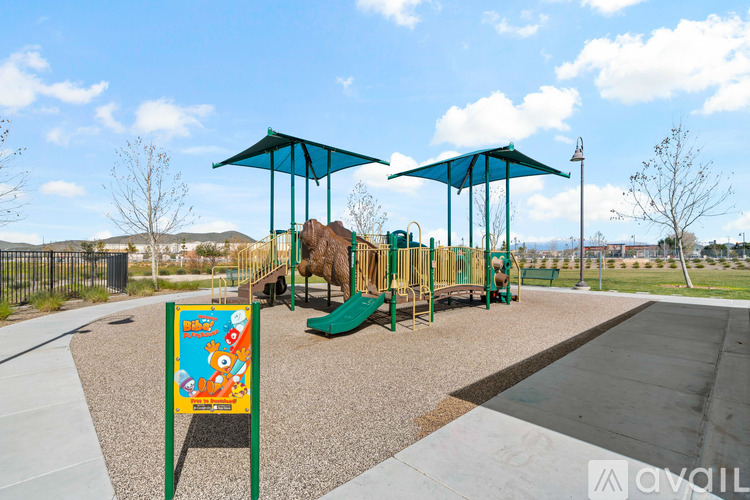 A playground with a slide, swings, and a sign with a cartoon character on it.