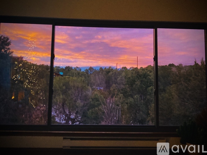 A view of a sunset through a window with trees and buildings in the distance.