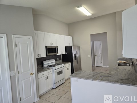 A kitchen with white cabinets and appliances, a marble countertop, and a tiled floor.
