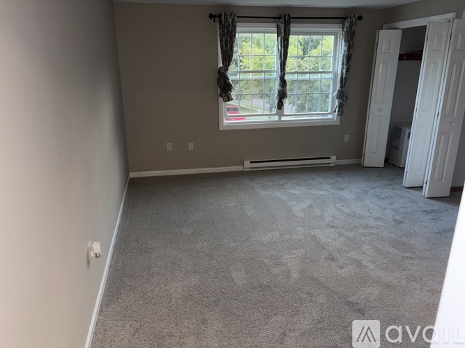 A room with a carpeted floor and a window with curtains.