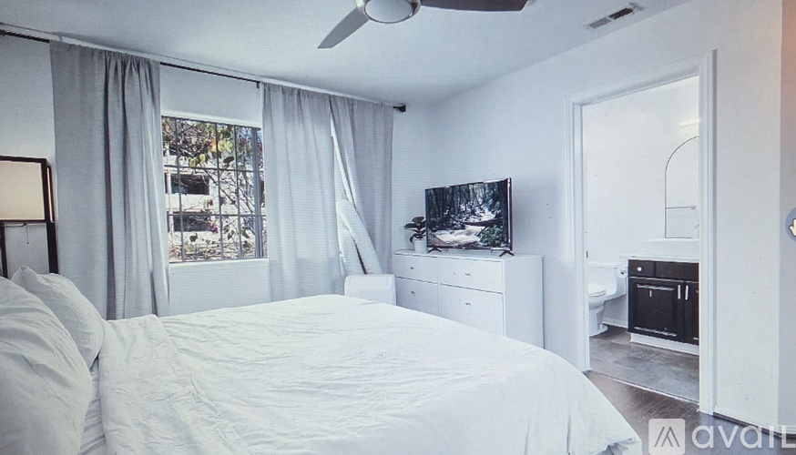 A bedroom with a large bed, a window with curtains, and a television on the dresser.
