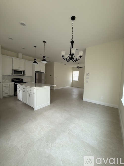 A large, empty living space with a kitchen area and a chandelier hanging from the ceiling.