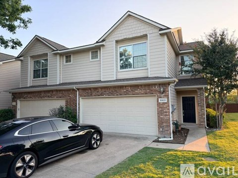 A black car is parked in front of a two-story house with a garage.
