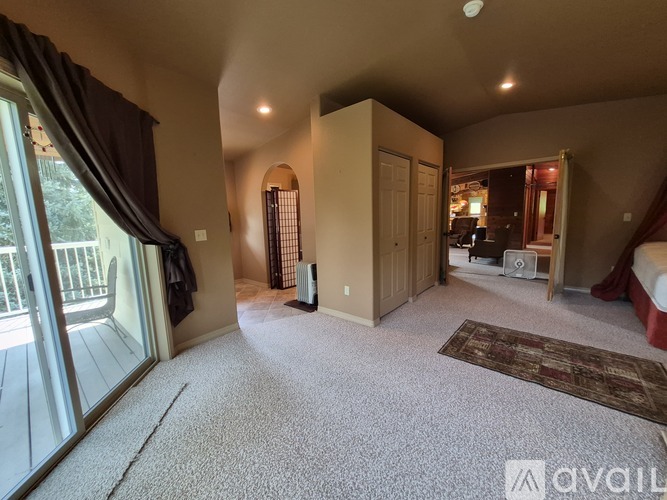 A spacious room with a carpeted floor and a large window with curtains.