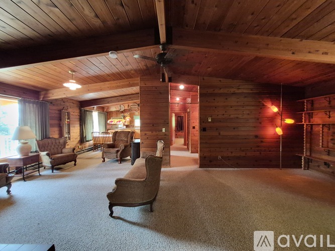 A living room with wooden walls and ceiling, furnished with a couch, armchairs, and a coffee table.