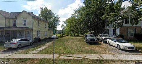 A street view of a residential area with houses and cars parked on the side.
