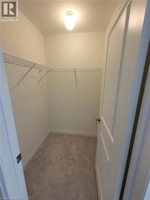 A small, empty bedroom with a carpeted floor and a single light bulb on the ceiling.