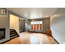 A spacious living room with wooden floors and a large window with a wooden blind.