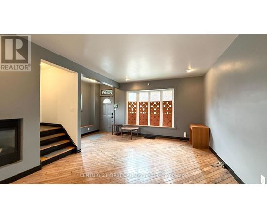 A spacious living room with wooden floors and a large window with a wooden blind.
