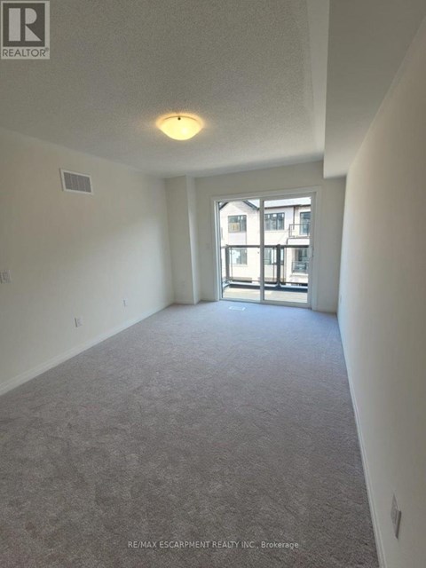 A large, empty room with a carpeted floor and a window with a view of a building outside.