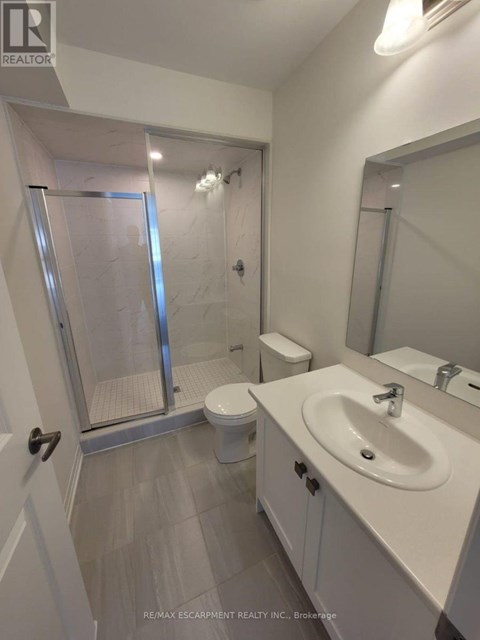 A white bathroom with a toilet, sink, and walk-in shower.