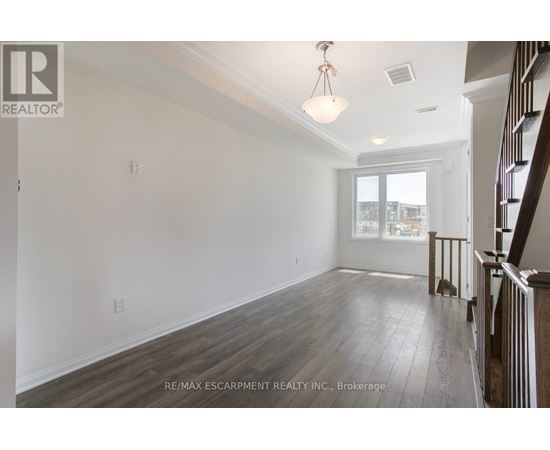 A spacious room with wooden flooring and white walls, with a window and a door visible.