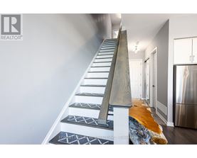 A staircase with a wooden handrail and patterned treads leads to a brightly lit hallway.