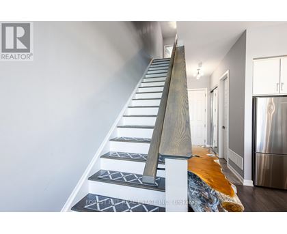 A staircase with a wooden handrail and patterned treads leads to a brightly lit hallway.