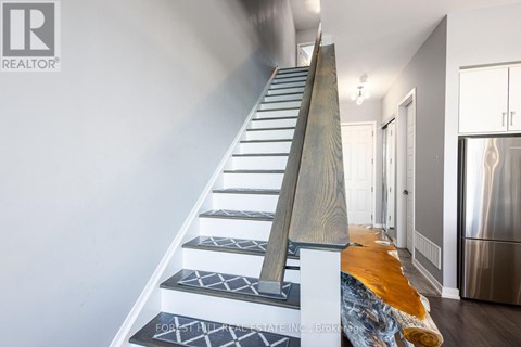 A staircase with a wooden handrail and patterned treads leads to a brightly lit hallway.