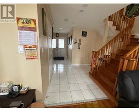 A hallway with a staircase on the right and a desk with a laptop on the left.