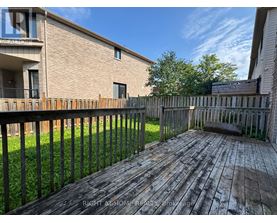A wooden deck with a black railing in front of a brick building.