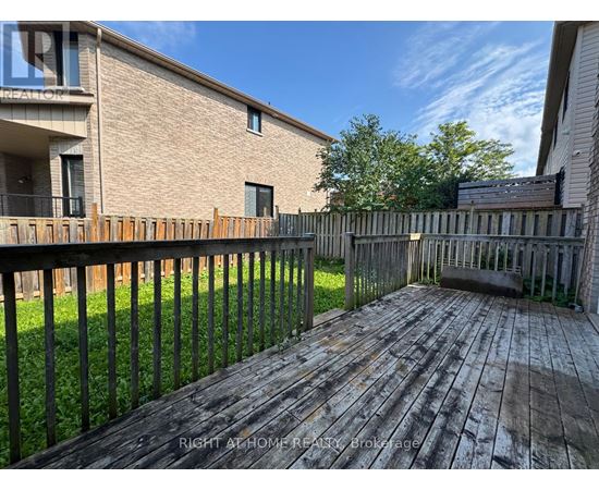 A wooden deck with a black railing in front of a brick building.