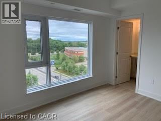 A room with a view of a parking lot and trees through a window.