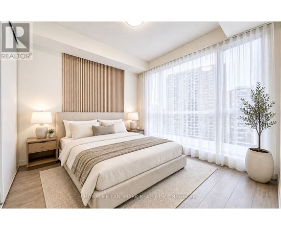 A bedroom with a large bed, a nightstand with a lamp, and a potted plant.