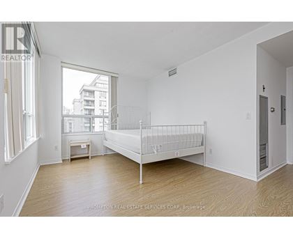 A white bedroom with a bed, nightstand, and window.