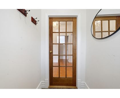 A white wall with a brown door and a mirror on the wall.