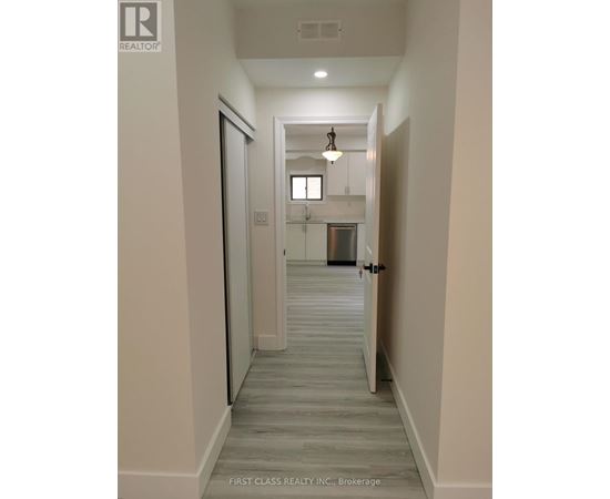 A hallway with a door on the left and a kitchen in the distance.