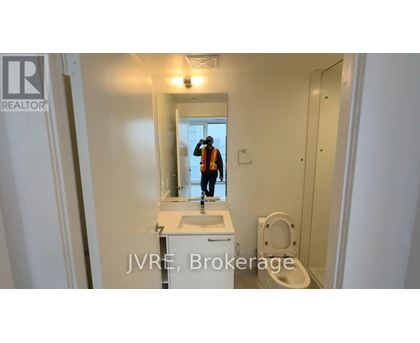 A bathroom with a sink, toilet, and a person in the background.