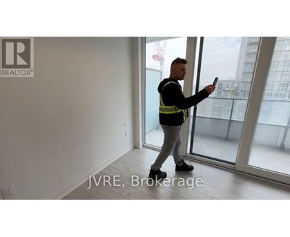 A man in a high visibility vest is holding a tablet in a room with a view of a construction site outside the window.