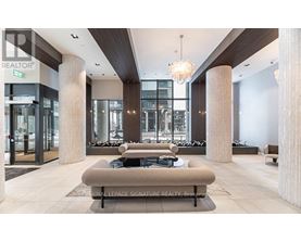 A modern lobby with a large sofa and pillows, a chandelier, and a glass wall.