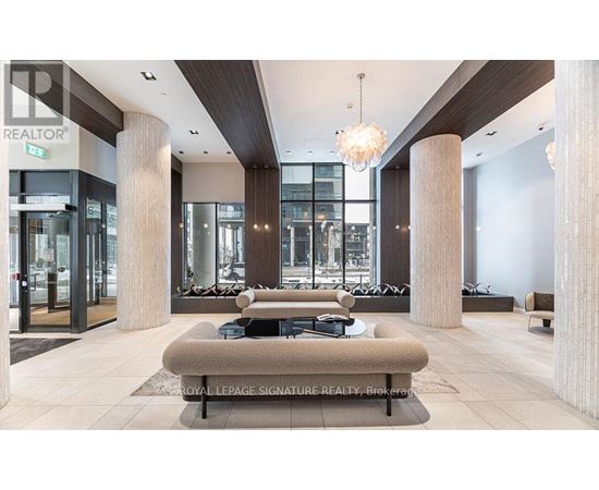 A modern lobby with a large sofa and pillows, a chandelier, and a glass wall.