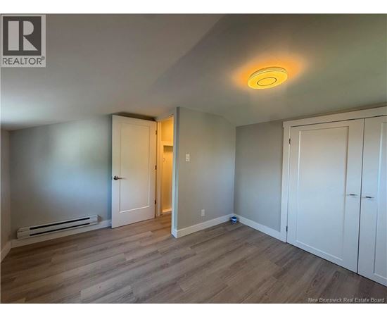 A room with a wooden floor and white walls, with a door on the left and a cabinet on the right.