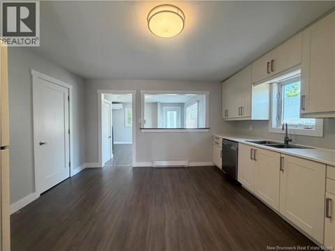 A spacious kitchen with white cabinets and a wooden floor.