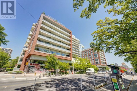 A tall building with a red and white facade stands in front of a tree-lined street.