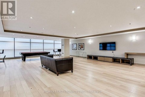 A spacious living room with a dark brown sofa and a television mounted on the wall.