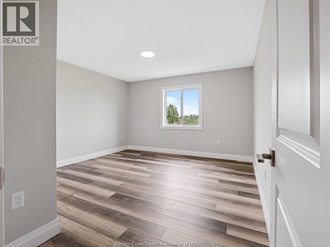 A room with wooden flooring and a window showing trees outside.