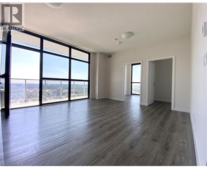 A spacious room with wooden flooring and large windows overlooking the city.