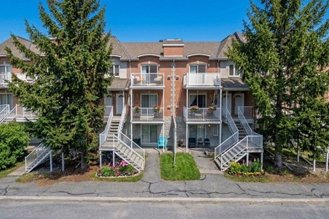 A large apartment complex with multiple balconies and trees in front.