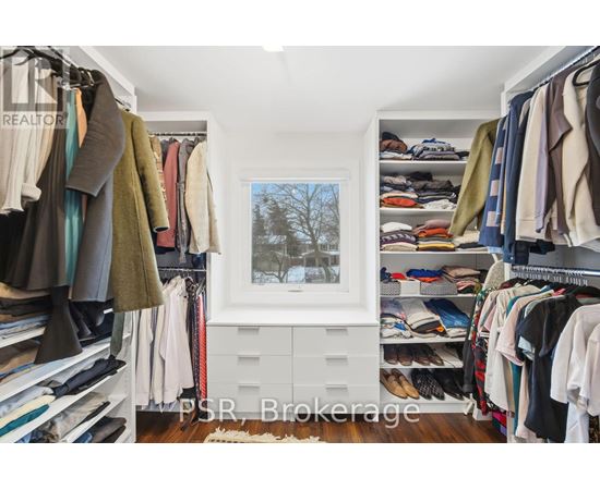A room with a window and a view of trees outside, with clothes hanging on racks and shelves.