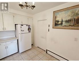 A kitchen with white cabinets and a fridge with a painting on the wall.