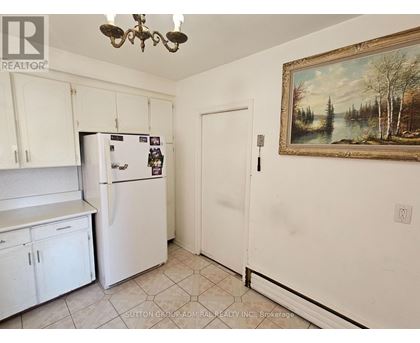 A kitchen with white cabinets and a fridge with a painting on the wall.