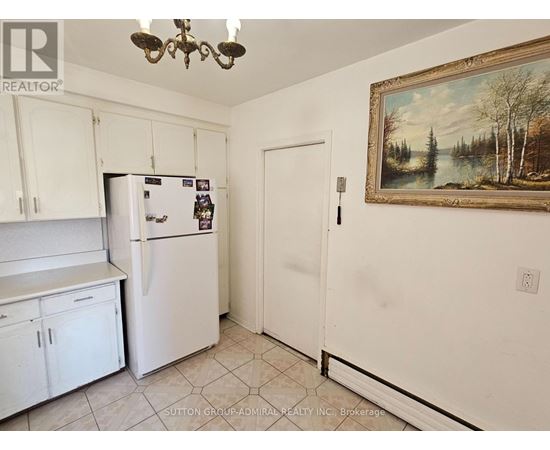 A kitchen with white cabinets and a fridge with a painting on the wall.