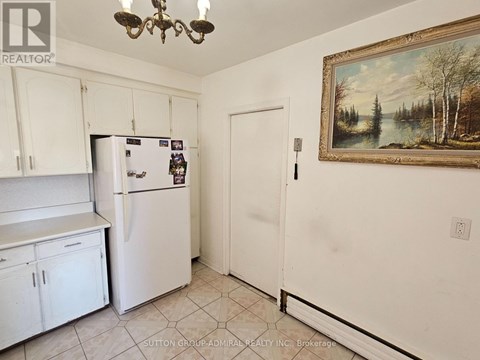 A kitchen with white cabinets and a fridge with a painting on the wall.