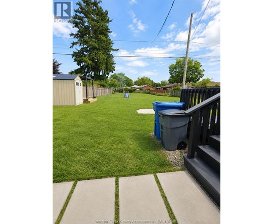 A backyard with a blue trash can and a wooden fence.
