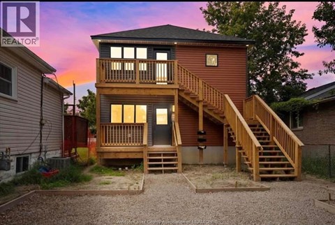 A two-story wooden house with a balcony and stairs leading to the upper level.